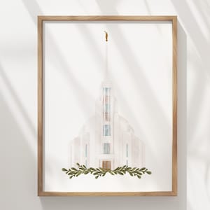 Può includere: Stampa ad acquerello di un tempio bianco con un'alta guglia, incorniciata in legno chiaro. Una statua dorata sovrasta la guglia. Il tempio ha accenti blu e marroni. Una ghirlanda di foglie verdi adorna la base del tempio. La stampa è esposta su un muro bianco.