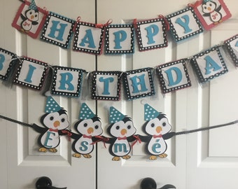 Pode incluir: Uma faixa de aniversário com as palavras "Happy Birthday" em letras azuis em quadrados brancos com bolinhas pretas. A faixa é decorada com recortes de pinguins usando chapéus de festa e segurando letras que soletram "Esme".