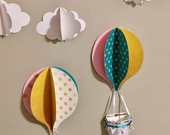 May include: Two paper hot air balloons with baskets hanging below. The balloons are decorated with pink, yellow, teal, and gold polka dots and hearts. The balloons are attached to a white wall with white paper clouds.