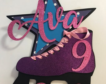 May include: Purple roller skate cake topper with pink glitter and a pink ribbon. The skate has a blue and white star with the name Ava on it and the number 9 on the side.