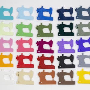 May include: A collection of colorful sewing machine cutouts in various shades, including blue, green, pink, red, orange, and yellow. The sewing machines are arranged in a grid pattern against a white background, showcasing a variety of hues.