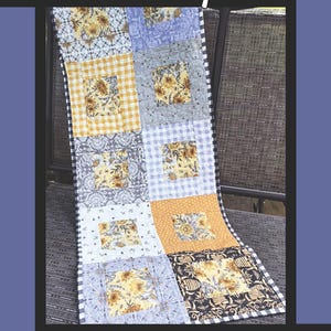 May include: A handmade quilt with a patchwork design featuring squares of floral and patterned fabrics in yellow, blue, gray, and white. The quilt has a black and white checkered border. The word "Honey" is at the top.
