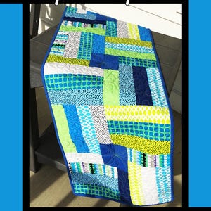 May include: A colorful quilt with a blue border, featuring various patterns in shades of blue, green, white, and black. The quilt has the text "Spin Cycle" and the names "Tricia Lynn Maloney" and "Orphan Quilt Designs".