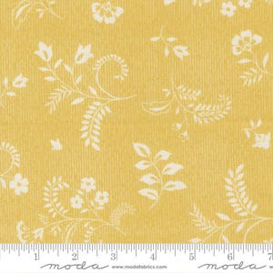 May include: Yellow fabric with a cream-colored floral pattern. The design features various flowers, leaves, and vines. The fabric has a textured appearance and a ruler along the bottom edge.