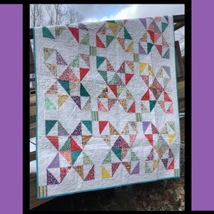 May include: A handmade quilt with a white background and colorful patchwork triangles. The quilt features a variety of fabrics in red, green, yellow, and purple. The word "Twinkle" is at the top, with the designer's name and design name at the bottom.