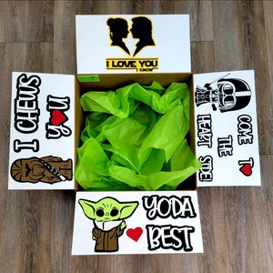 May include: A white gift box with a Star Wars theme. The box is open and filled with green tissue paper. The sides of the box have different Star Wars characters and sayings, including "I Chews You", "Come to the Dark Side", "Yoda Best", and "I Love You, I Know".