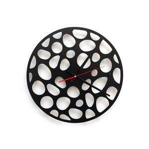 Peut inclure: Horloge murale noire avec un design unique présentant un motif découpé circulaire de cercles de différentes tailles. L'horloge a des aiguilles noires et une aiguille des secondes rouge.