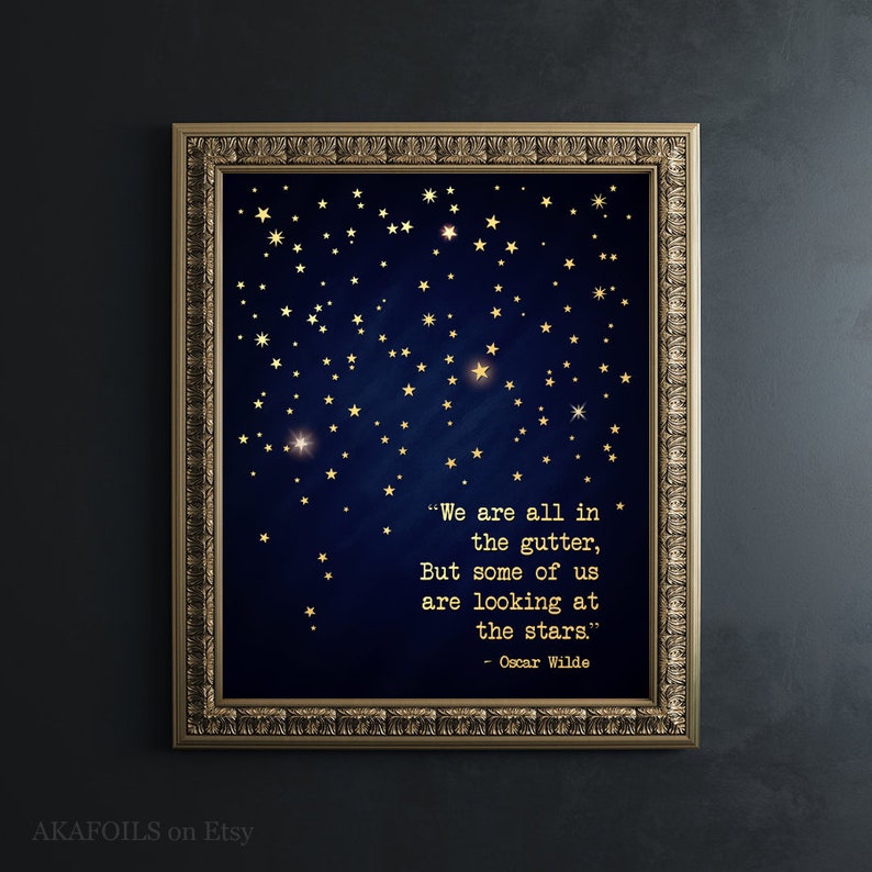 May include: A gold framed print with a dark blue background and gold stars. The print features a quote by Oscar Wilde: "We are all in the gutter, But some of us are looking at the stars."