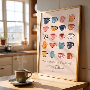 May include: A framed wall art print featuring a grid of twenty colorful illustrated coffee mugs in various patterns and colors, with the text "Pour yourself a cup of ambition." and a signature below, displayed in a gold-colored frame.