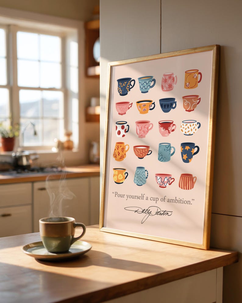 May include: A framed wall art print featuring a grid of twenty colorful illustrated coffee mugs in various patterns and colors, with the text "Pour yourself a cup of ambition." and a signature below, displayed in a gold-colored frame.