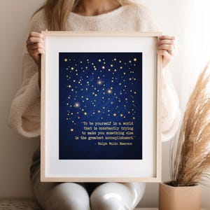 May include: A blue and gold printable wall art print with a quote by Ralph Waldo Emerson: "To be yourself in a world that is constantly trying to make you something else is the greatest accomplishment."