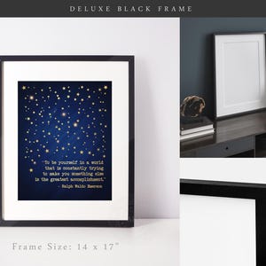 May include: A black framed print with a blue background and gold stars. The print features a quote by Ralph Waldo Emerson: "To be yourself in a world that is constantly trying to make you something else is the greatest accomplishment." The frame is 14 inches by 17 inches.