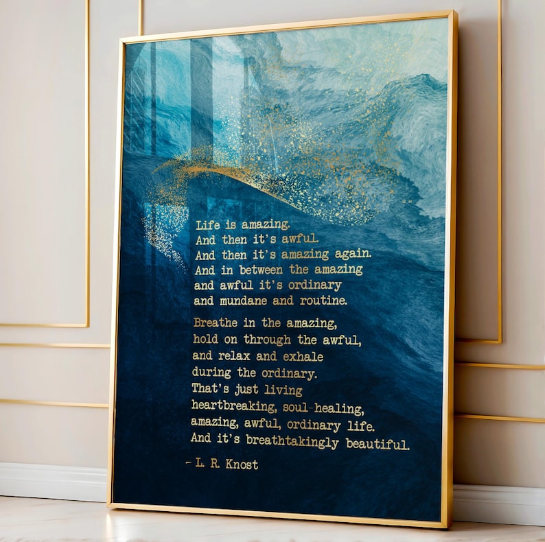 May include: A vertical rectangular wall art print in a thin gold frame featuring a deep blue and teal abstract watercolor background with gold glitter accents. The text reads: Life is amazing. And then it's awful. And then it's amazing again. - L. R. Knost.