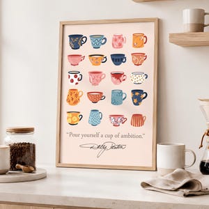May include: A framed wall art print featuring a grid of twenty illustrated colorful coffee mugs in various patterns and hues on a light pink background. Below the mugs, the text reads "Pour yourself a cup of ambition." with a signature underneath.