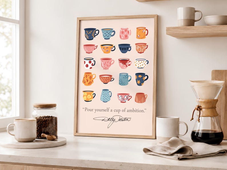 May include: A framed wall art print featuring a grid of twenty illustrated colorful coffee mugs in various patterns and hues on a light pink background. Below the mugs, the text reads "Pour yourself a cup of ambition." with a signature underneath.