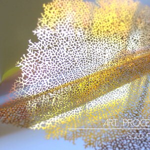 May include: A close-up of a gold foil design with a delicate, intricate pattern. The foil is folded and layered, creating a three-dimensional effect. The text "ART PROCESS GOLD FOIL" is visible at the bottom of the image.
