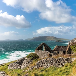Puede incluir: Un edificio de piedra con un techo parcial que domina un océano azul con olas blancas. El edificio está en ruinas y tiene una abertura de ventana. El océano está en el fondo y hay colinas verdes en la distancia.