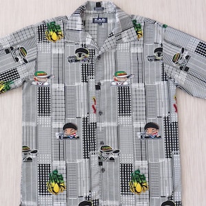 May include: Short-sleeved button-down shirt with a black and white geometric pattern. The shirt features cartoon graphics of a person wearing a cap and sunglasses, and a pineapple. The shirt has a collared neckline.