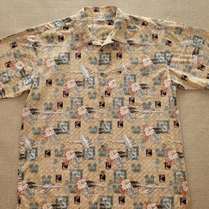 May include: A beige short-sleeved button-down shirt with a tropical print featuring aeroplanes, flowers, and leaves.