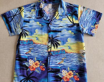 Puede incluir: Camisa de manga corta con botones con estampado de escena de playa tropical. La camisa presenta un diseño vibrante con palmeras, surfistas y flores coloridas en tonos de azul, amarillo y morado.