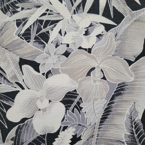Może przedstawiać: Tkanina z monochromatycznym nadrukiem botanicznym przedstawiającym duże kwiaty storczyka i liście palm tropikalnych w odcieniach czerni, bieli i szarości. Wz&oacute;r ukazuje gęsty, nakładający się układ liści i kwiat&oacute;w o wyraźnej teksturze.