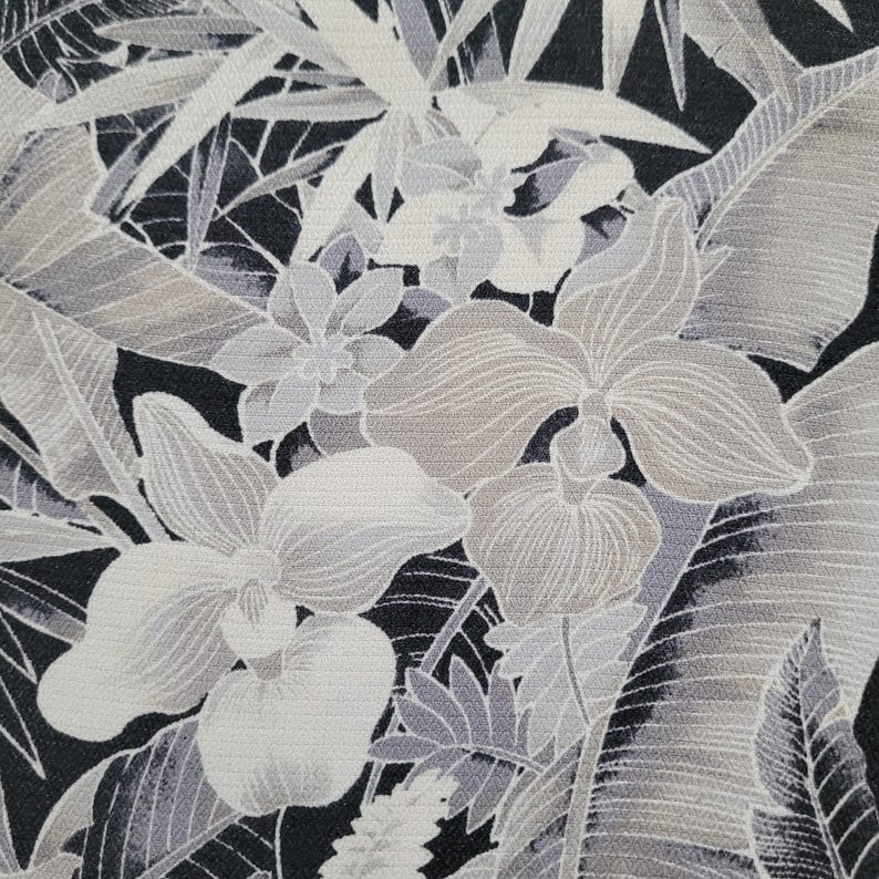 Może przedstawiać: Tkanina z monochromatycznym nadrukiem botanicznym przedstawiającym duże kwiaty storczyka i liście palm tropikalnych w odcieniach czerni, bieli i szarości. Wz&oacute;r ukazuje gęsty, nakładający się układ liści i kwiat&oacute;w o wyraźnej teksturze.