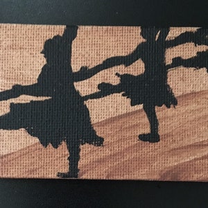 Puede incluir: Una pintura de dos bailarines en silueta sobre un fondo de lienzo marrón.