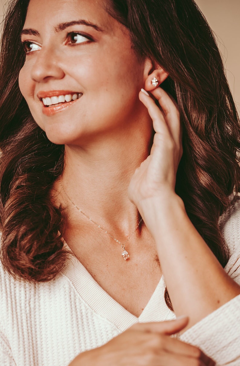 Herkimer Diamond Stud Earrings worn by a smiling woman with a matching Herkimer Diamond necklace. Quartz crystals wrapped three times in gold wire for completed post earrings. The quartz crystals are transparent, colorless, and naturally faceted.