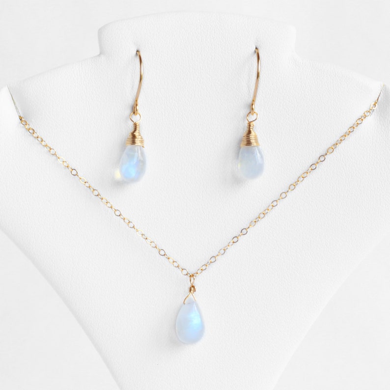 Puede incluir: Un conjunto de collar y pendientes de oro con colgantes de piedra lunar en forma de l&aacute;grima. El collar tiene una cadena delicada y los pendientes son de estilo colgante.