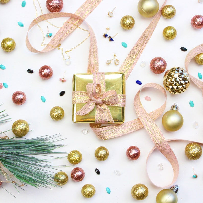 A small gift-wrapped jewelry box in gold wrapping paper with a pink sparkling bow.