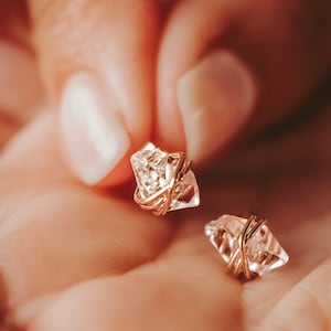 Herkimer Diamond Stud Earrings in the palm of a woman with manicured nails. Quartz crystals wrapped three times in gold wire for completed post earrings. The quartz crystals are transparent, colorless, naturally faceted, and pointed on both ends.