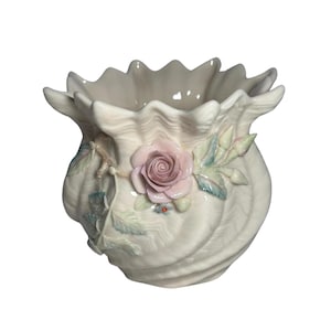 May include: A cream-colored ceramic vase with a scalloped rim and a shell-like, ribbed texture. The exterior is decorated with a three-dimensional sculpted pink rose, green leaves, and small buds attached to a textured branch-like stem.