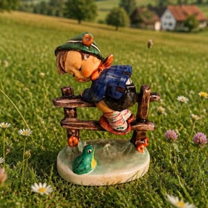 May include: A ceramic figurine of a child wearing a green hat, blue jacket, and striped socks, leaning over a brown wooden fence. A small green frog sits on the circular base below the fence, which features painted red accents on the posts.