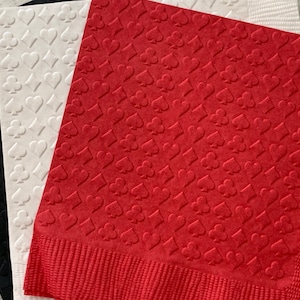Puede incluir: Tres servilletas de papel con un patr&oacute;n repetido de palos de cartas de juego rojos, blancos y negros. Las servilletas est&aacute;n dobladas en tres y tienen una superficie texturizada.