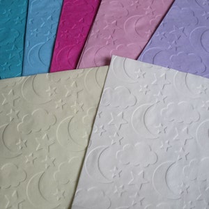 May include: Assortment of embossed paper sheets with a moon and star pattern. The sheets are in various colors, including blue, pink, purple, and white.