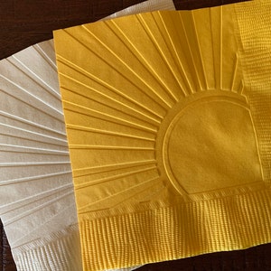 May include: Two paper napkins with an embossed sun design. One napkin is white and the other is yellow.