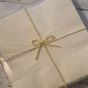May include: A set of white paper napkins with a sunburst design, tied together with yellow and white twine.