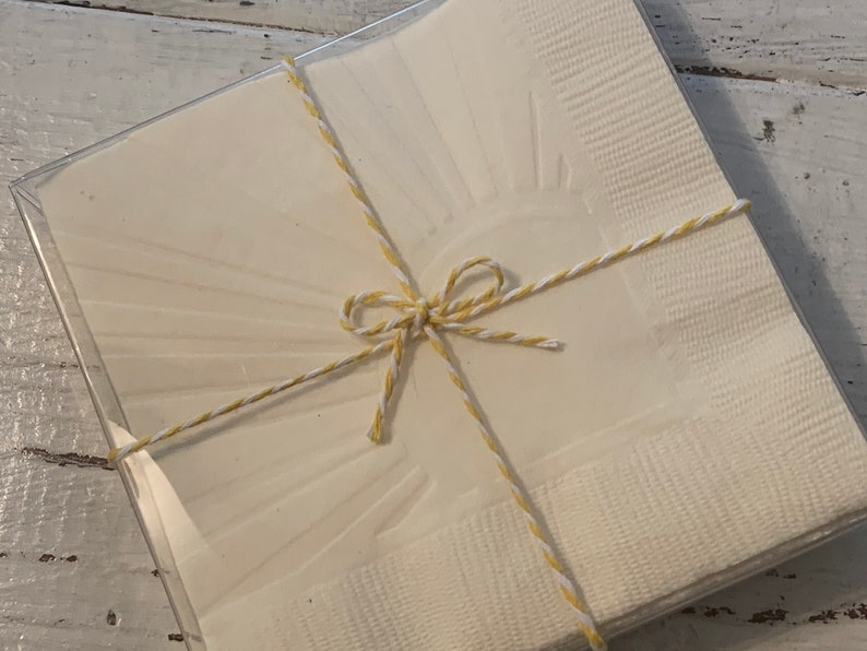 May include: A set of white paper napkins with a sunburst design, tied together with yellow and white twine.
