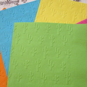 Puede incluir: Cuatro servilletas de diferentes colores con un patrón de cactus. Las servilletas son naranja, azul, verde y rosa.