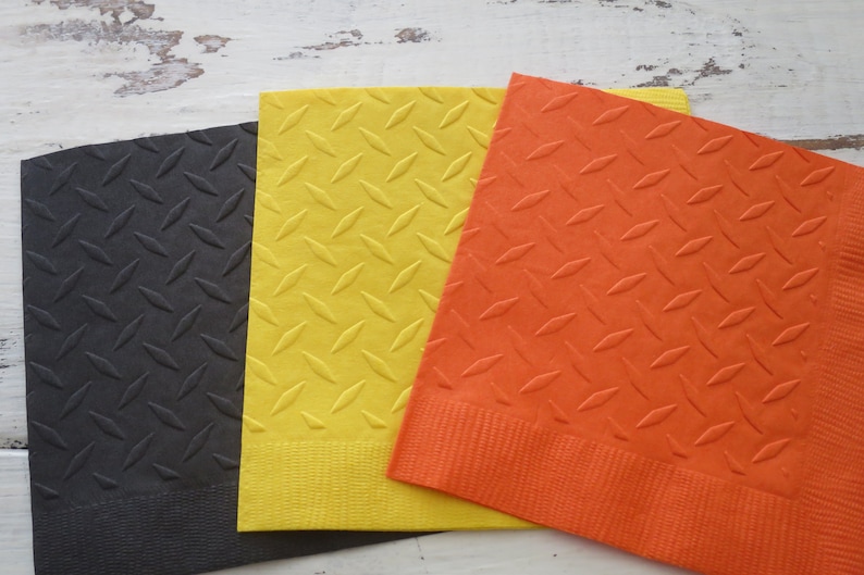 May include: Three square napkins with a diamond pattern. The napkins are black, yellow, and orange.