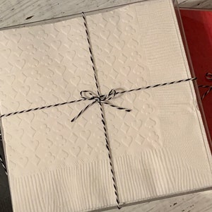 Puede incluir: Tres cajas de regalo envueltas en papel blanco, negro y rojo con lazos de cuerda negra y blanca. La caja blanca tiene un patr&oacute;n de corazones.