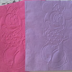 May include: Pink and lilac paper napkins with an embossed Minnie Mouse design. The napkins have a textured surface, suitable for parties or themed events. The Minnie Mouse design includes her signature bow and polka-dot dress.