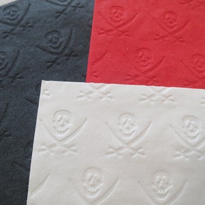 May include: Three sheets of paper with a repeating pattern of embossed skull and crossbones. The paper is black, red, and white.
