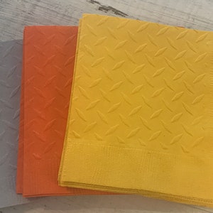 May include: Three stacks of paper napkins with a diamond pattern. The napkins are gray, orange, and yellow.