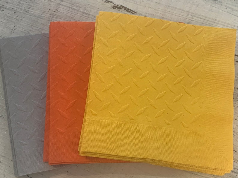 May include: Three stacks of paper napkins with a diamond pattern. The napkins are gray, orange, and yellow.