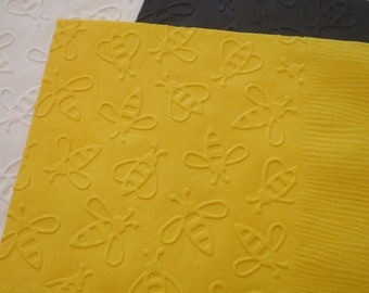 Könnte beinhalten: Gelbe Papier-Servietten mit einem sich wiederholenden, geprägten Muster von Bienen.