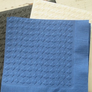 Puede incluir: Tres servilletas de papel con un patr&oacute;n en relieve de palos de cartas de juego. Las servilletas son de color negro, azul y blanco.