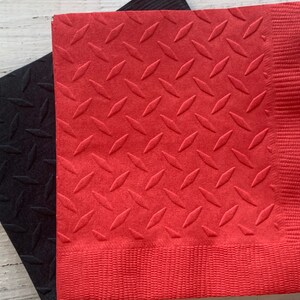May include: Two red and black paper napkins with a diamond pattern embossed on the surface. The napkins are folded and stacked on top of each other.
