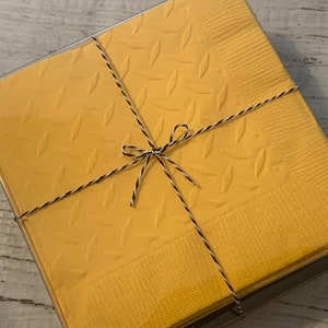 May include: A package of yellow napkins with a diamond pattern, tied with black and white twine.