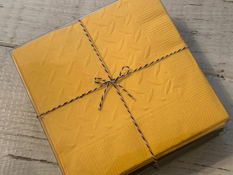 May include: A package of yellow napkins with a diamond pattern, tied with black and white twine.